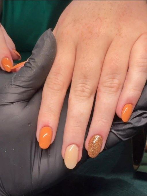 Short almond manicure in orange and nude with a gold glitter accent nail